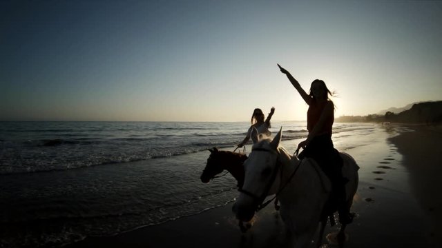Majestic horseback riders on sunset beach, slow motion