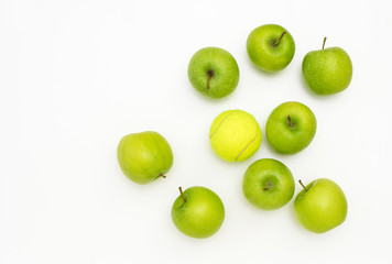 Juicy green apples lying on white background but one is different, the odd one out, an outsider, different and unlike the others because it is a tennis ball, concept of misfit