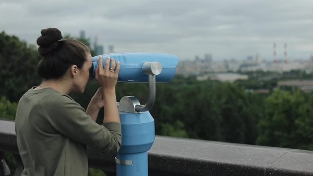 Side view of a beautiful girl watching the cityscape through tourist telescope