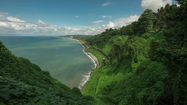 Mountains covered with trees and bushes, cliff to a stone beach and the sea with railway tracks and a tunnel, a botanical garden on a hilly locality