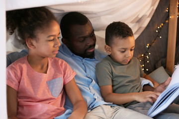 African American man reading bedtime story to his children at home