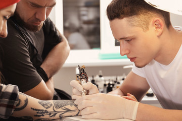 Professional tattoo master teaching young specialist in salon. Internship concept