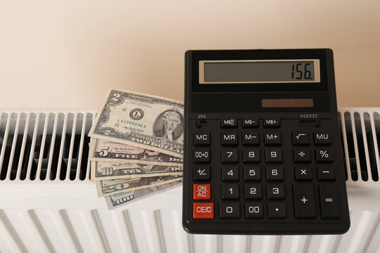 Heating radiator with calculator and money on color background