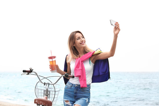 Attractive woman taking selfie near bicycle on sea coast
