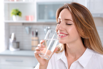 Young woman drinking clean water from glass in kitchen