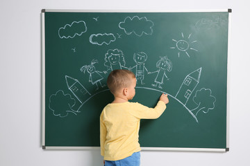 Little child drawing family with white chalk on blackboard