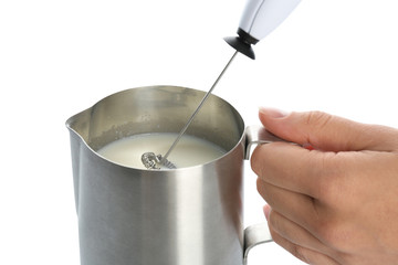 Woman using milk frother device in pitcher on white background, closeup