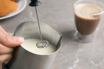 Woman using milk frother device in pitcher on table