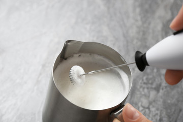 Woman using milk frother in pitcher on table, closeup