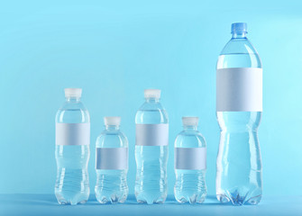 Different bottles of pure water with blank tags on color background