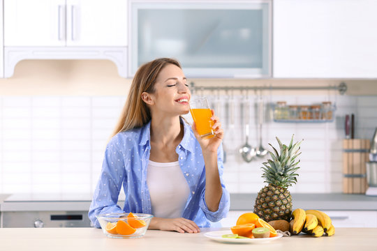 Woman with glass of orange juice at table in kitchen. Healthy diet