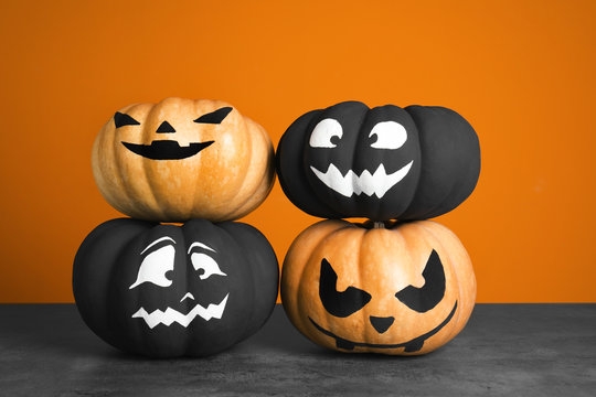 Pumpkins with scary faces on table against color background. Halloween decor