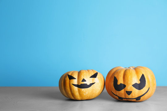 Pumpkins with scary faces on table against color background, space for text. Halloween decor