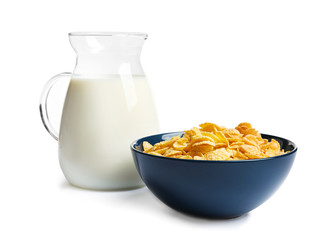 Bowl with crispy cornflakes and jug of milk on white background