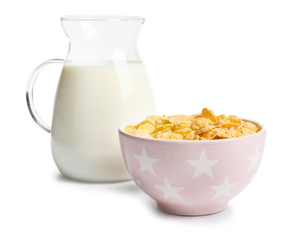 Bowl with crispy cornflakes and jug of milk on white background