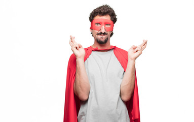 Young bearded super hero crossing fingers wishing for luck, with a hopeful, eager and excited expression. © kues1