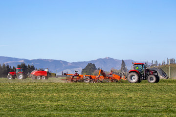 Red farm machinery at work in a rural field in Canterbury, New Zealand, raking and baling hay