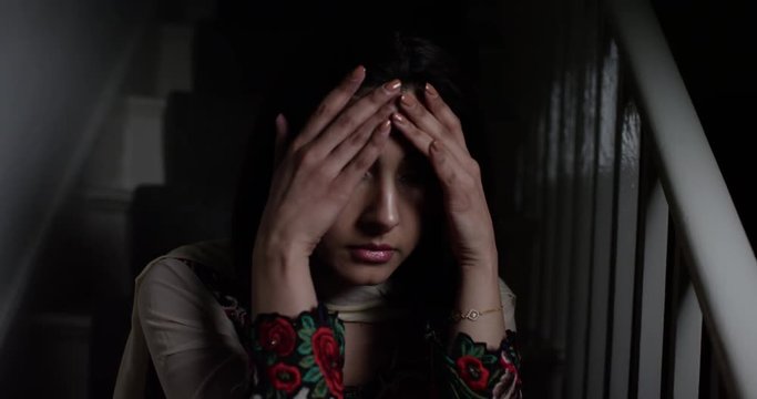 4K Young Indian woman sitting alone in the dark, dealing with emotional depression. Slow motion.