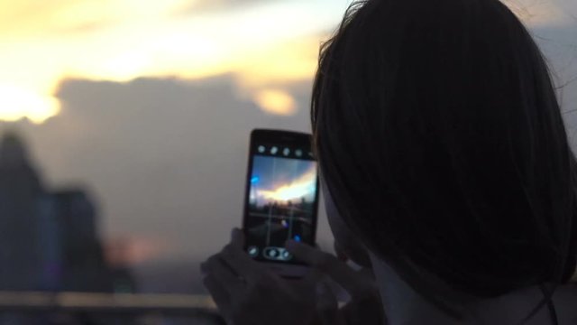 Woman taking photo of sunset with cellphone in skybar
