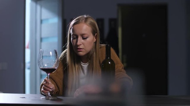 Wasted hopeless adult drunk woman in midlife crisis drinking wine while sitting alone at home. Abandoned lonely female in self-pity escaping problems and reality in alcohol abuse and alcoholism.