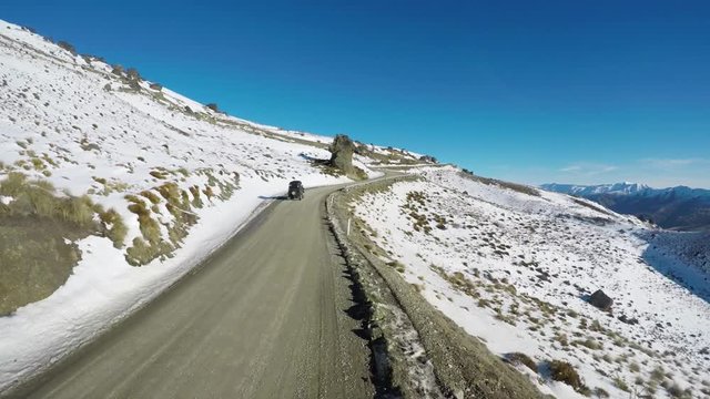 Wide aerial, car drives on mountain road in winter