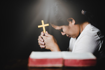 Woman hands praying with a cross and bible in a dark over wooden table