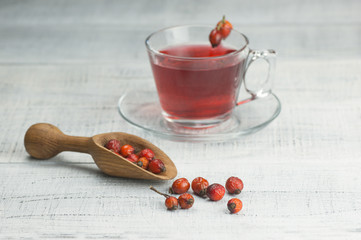 Dried rose hip cup of herbal tea medicinal plants on white black wooden vintage table with wooden shovel and rosehips. Dogrose background
