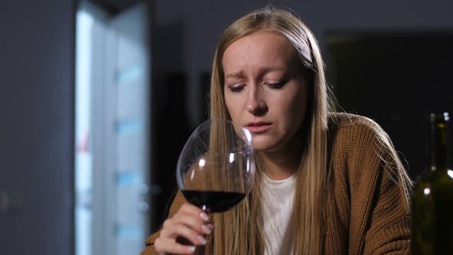 Abandoned emotionally stressed woman in tears drinking glass of red wine at home to relieve the pain after husband leave to younger female. Cheated wife after divorce in alcohol abuse crying indoors.