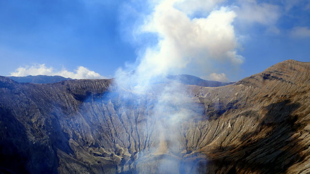 Kraterrand des Vulkans Bromo mit aufsteigendem Rauch in den blauen Himmel in Java