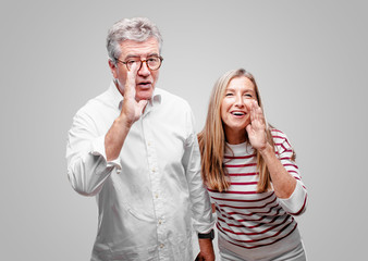 senior cool husband and wife leaning forward and whispering a secret with a serious and surprised...