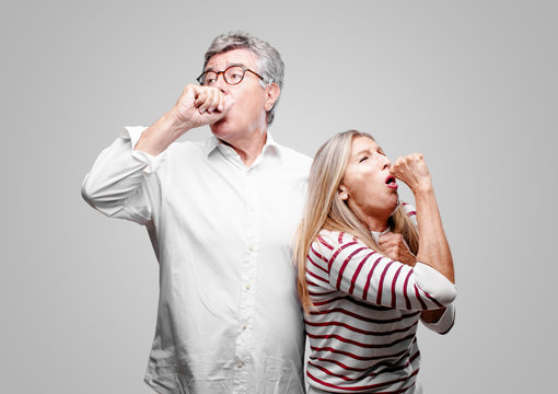 senior cool husband and wife Coughing, suffering a winter illness such as a cold or the flu, feeling unwell and feverish.