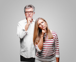 senior cool husband and wife with a goofy, dumb, silly look, feeling shocked and confused at a...