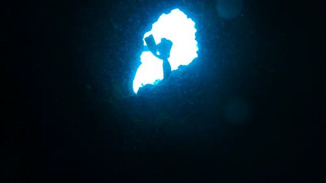 POV, divers swim through cave in slow motion