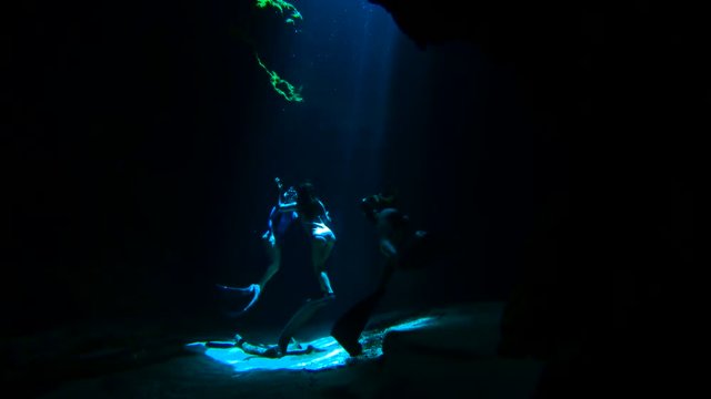 Slow motion, divers swim in cave