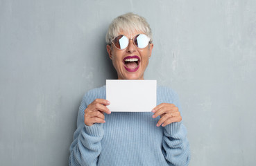 senior cool woman holding an empty placard against grunge cement wall.