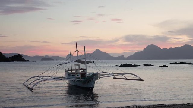Traditional filipino bangka boat on calm waters at dusk with pink and orange sky