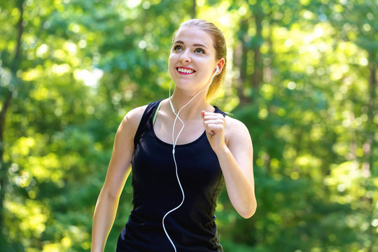 Athletic young woman jogging on a bright summer day in the forest