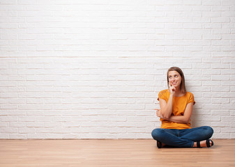 young pretty woman thinking or looking pensive to an empty place against brick wall background