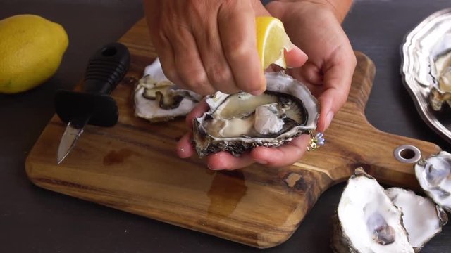 someones hands squising lemon on fresh raw oysters