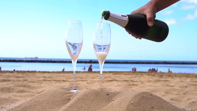 champagne on beach - someones hands pouring drink into the glasses, slow motion