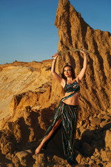 Oriental Beauty dancing belly dance with saber barefoot in the desert. Dangerous huriyah and heavenly pleasures. Portrait on a background of golden sand dunes at sunset