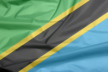 Fabric flag of Tanzania. Crease of Tanzanian flag background, A yellow-edged black diagonal band: the upper triangle is green and the lower triangle is blue.