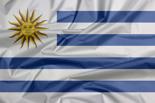 Fabric flag of Uruguay. Crease of Uruguayan flag background, horizontal stripes of white alternate with light blue and the Sun of May.