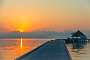 Wooden pier at tropical island resort at sunset time, Maldives. Vacations And Tourism Concept