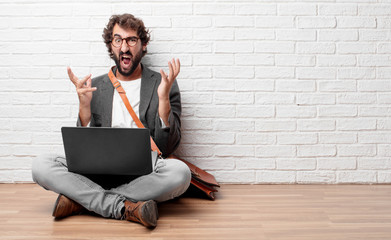 young man sitting on the floor looking angry, unhappy and frustrated, gesturing furiously and...