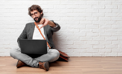 young man sitting on the floor with a dissenting, serious, stern expression, with thumbs down in...