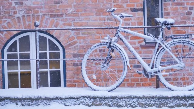 Winter day in city. Snow covered bicycle parked on streen.
