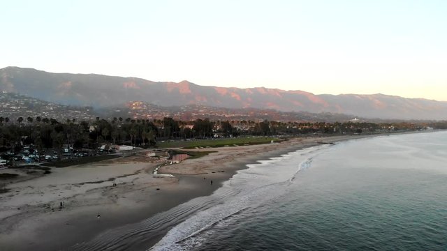 Aerial drone shot at sunset above a Pacific Ocean beach and marina looking over the the beautiful city of Santa Barbara and the hills of Monecito, California.