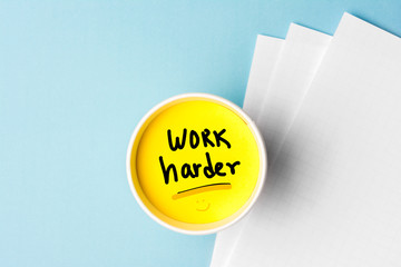 Work harder concept, handwriting message on cup with blue background and papers