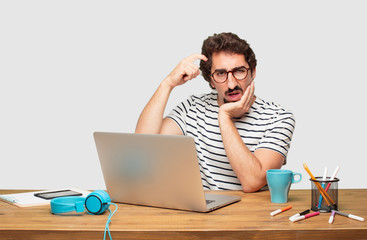 young bearded graphic designer with a laptop with a goofy, dumb, silly look, feeling shocked and...
